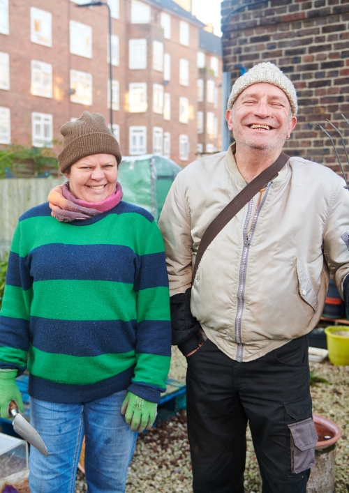 A smiling man and woman holding gardening tools