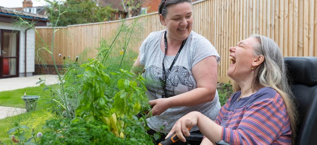 A Sanctuary Supported Living member of staff and a resident in a wheelchair laughing together whilst doing gardening