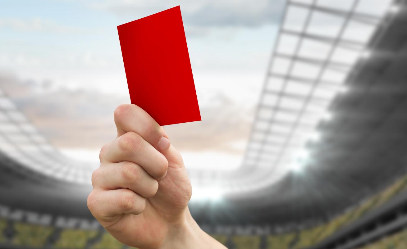 A hand holding up a red card in a stadium